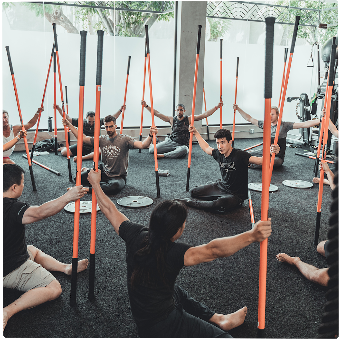Group of people sitting holding a training stick in each hand. performing the 90/90 movement.