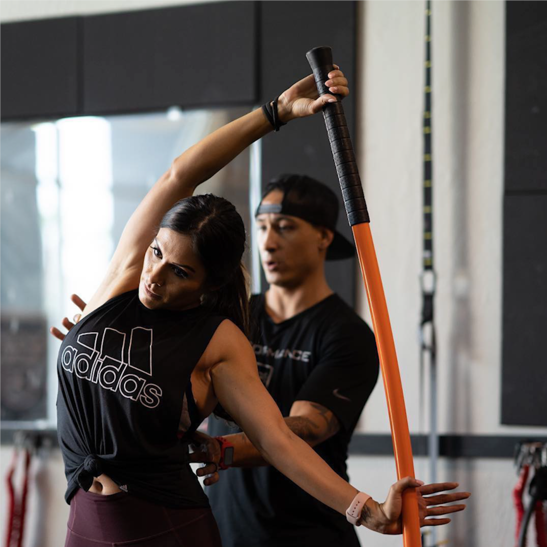 Woman performing a bow and arrow with a man providing assistance.