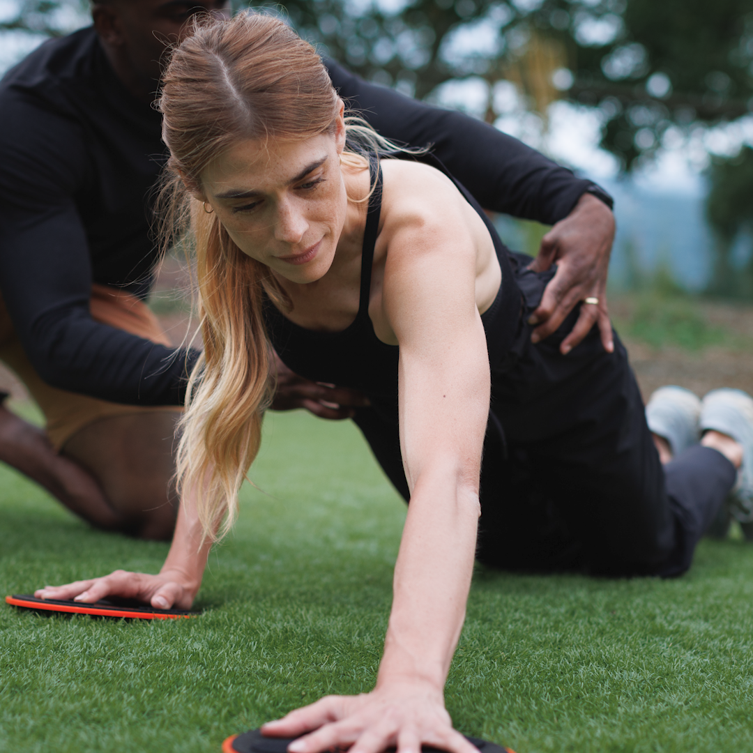 A female client performing a core exercise using the Stick Mobility TriSlider, focusing on dynamic stability, mobility, and core strength.