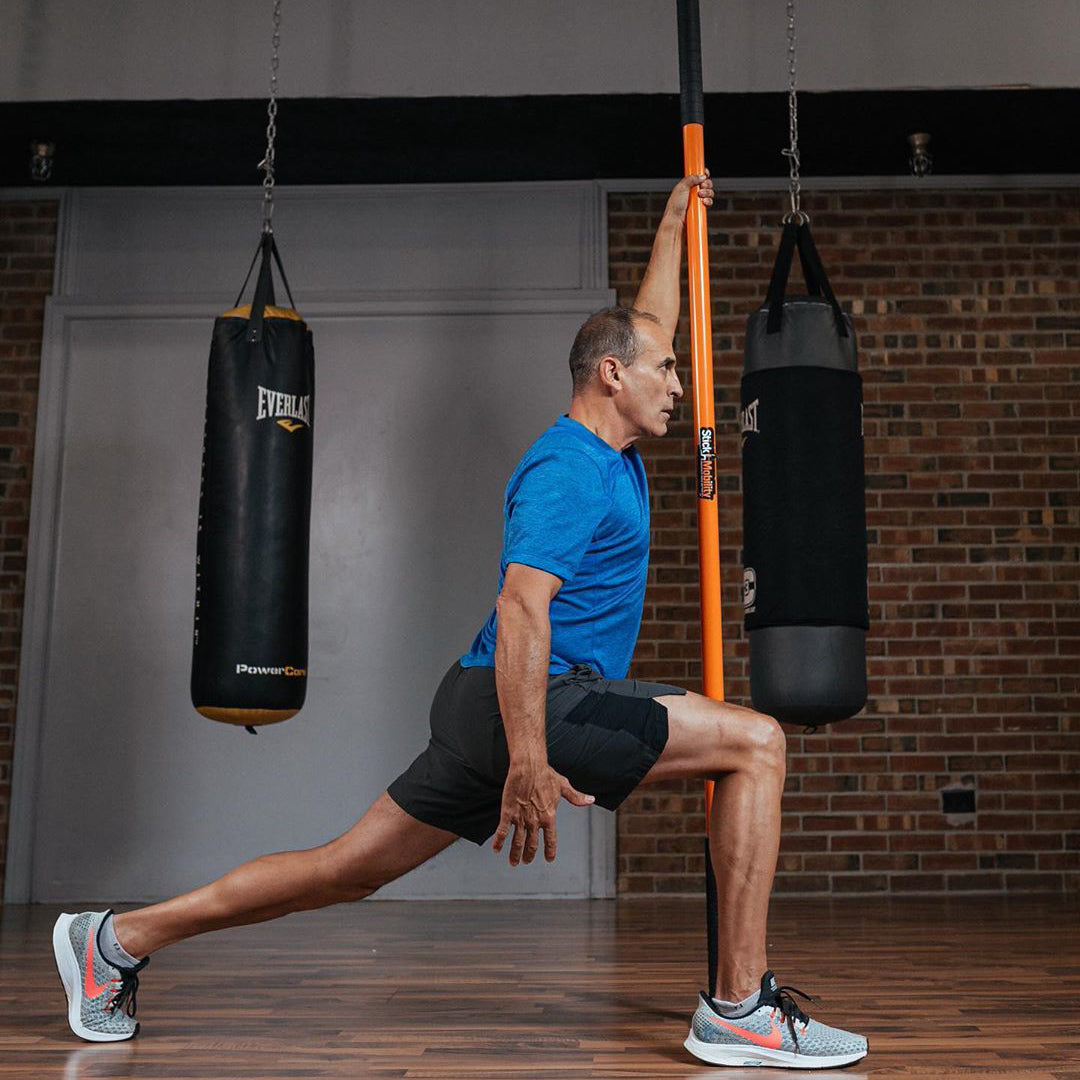 Man performing a split lunge monkey hang with a Stick Mobility Training Stick.