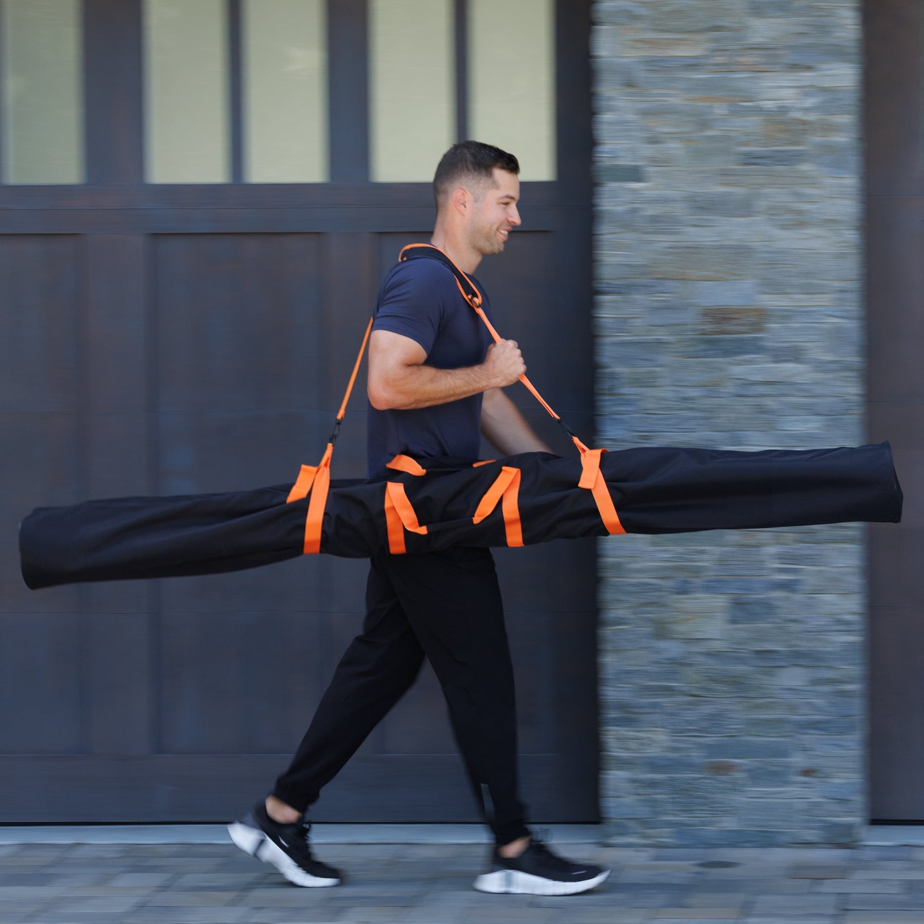 A male model in action carrying the Stick Mobility training stick carry bag, showcasing the bag’s portability and functionality for transporting training sticks during mobility workouts.