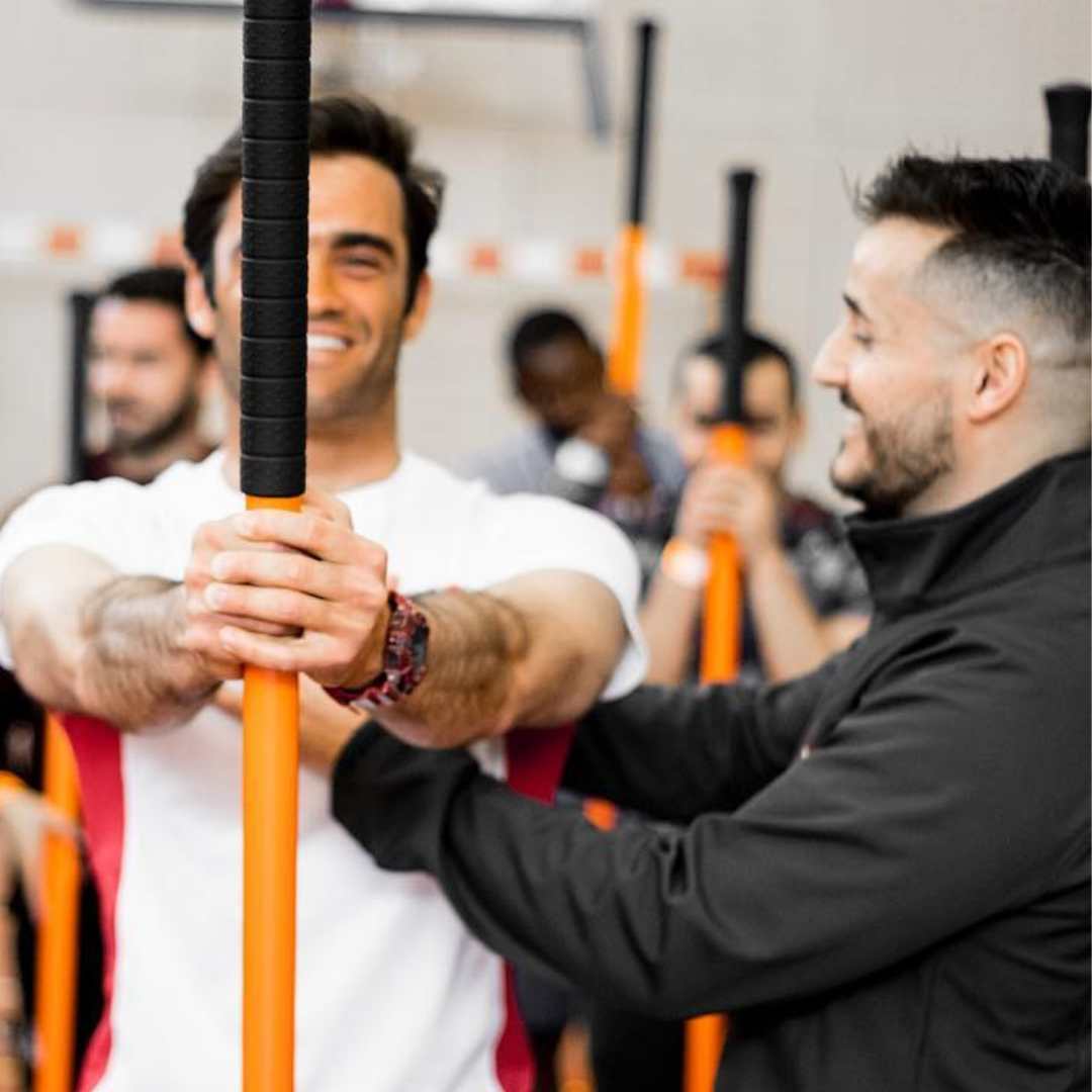Man holding the Training Stick in front of him while another man assists him with the movement.