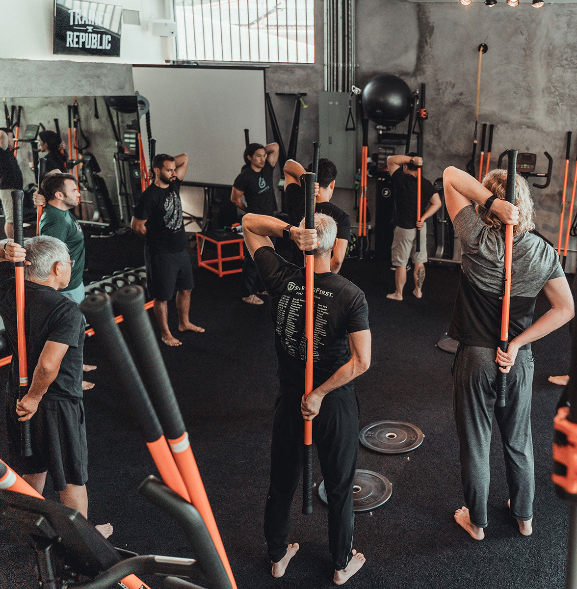 Group of people from the Stick Mobility certification performing a movement with the Training Stick behind their back, practicing pulling the stick apart.