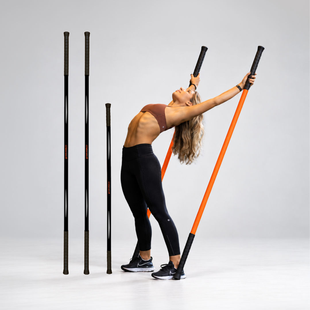 A woman in a brown sports bra and black leggings performs a movement using Stick Mobility Training Sticks. The black Training Sticks stand next to the model performing the movement.