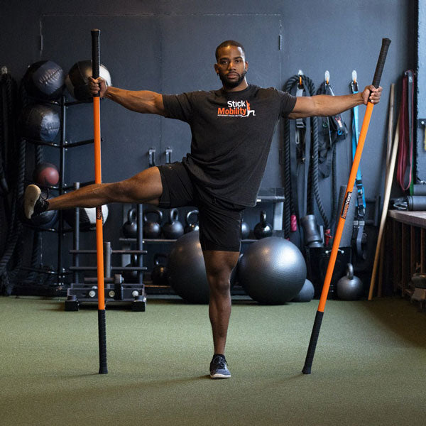 Man exercising with two Stick Mobility training sticks, balancing on one leg and the other leg held out to his side.