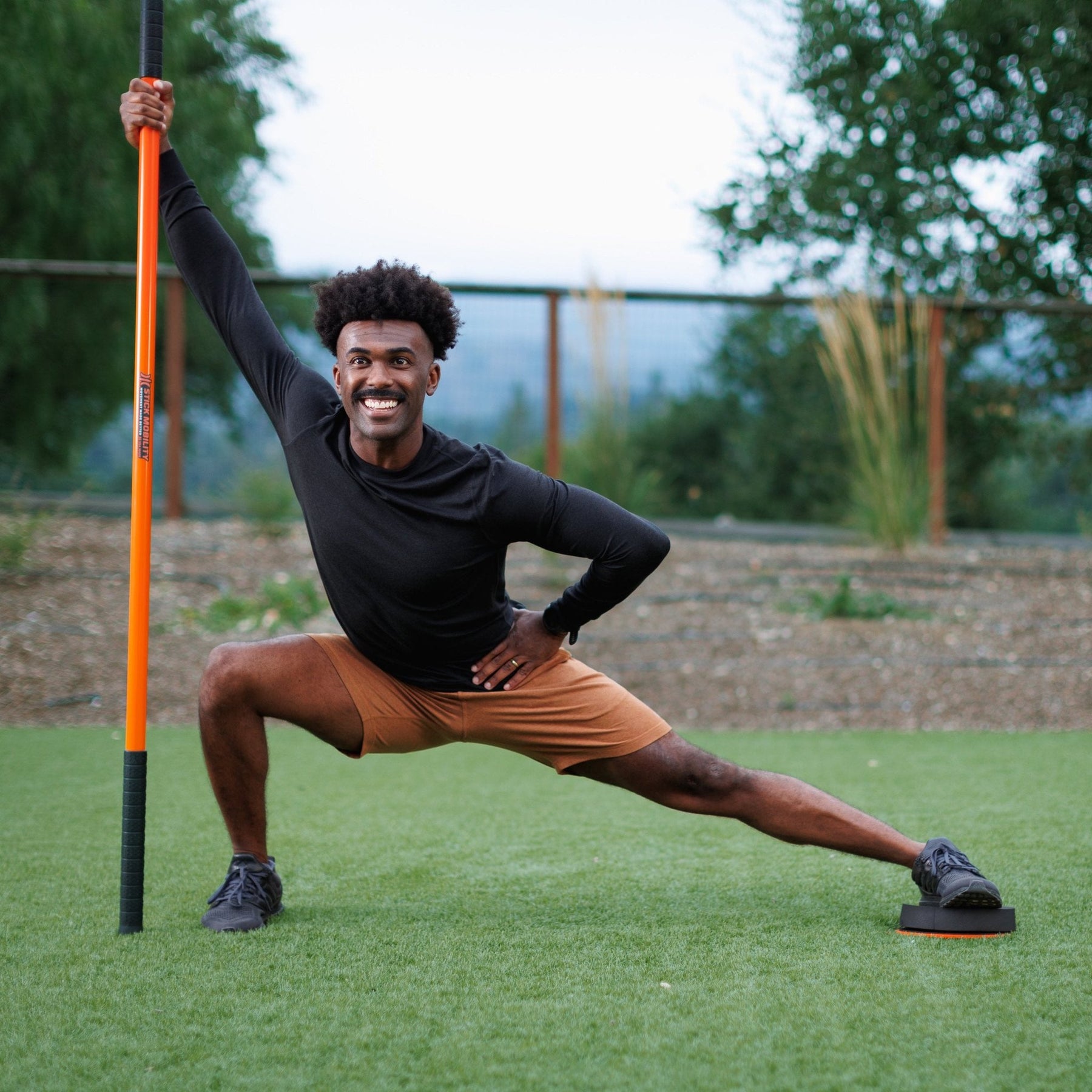 Man in a side lunge using the training stick for balance.