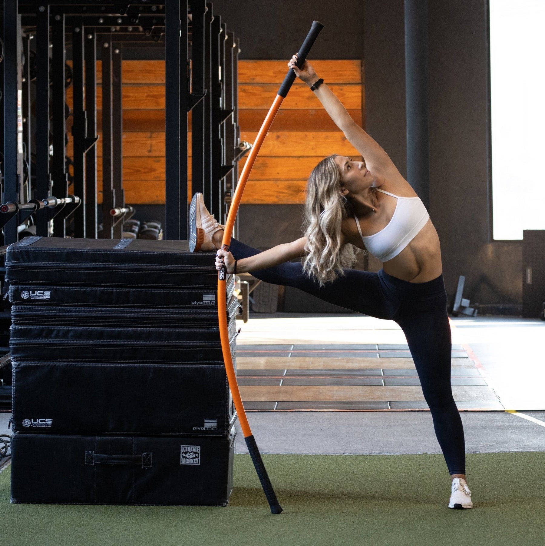Woman standing with one leg on stretched out on top of a box performing the stick mobility bow and arrow.