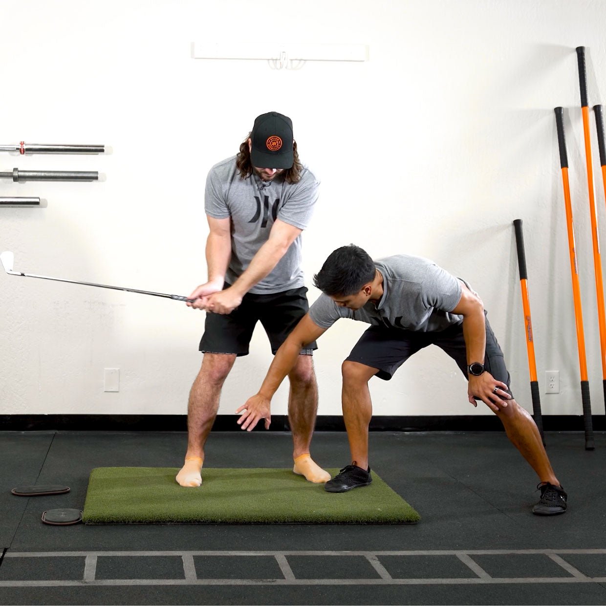 Man swinging golf club while other man is providing visual feedback.