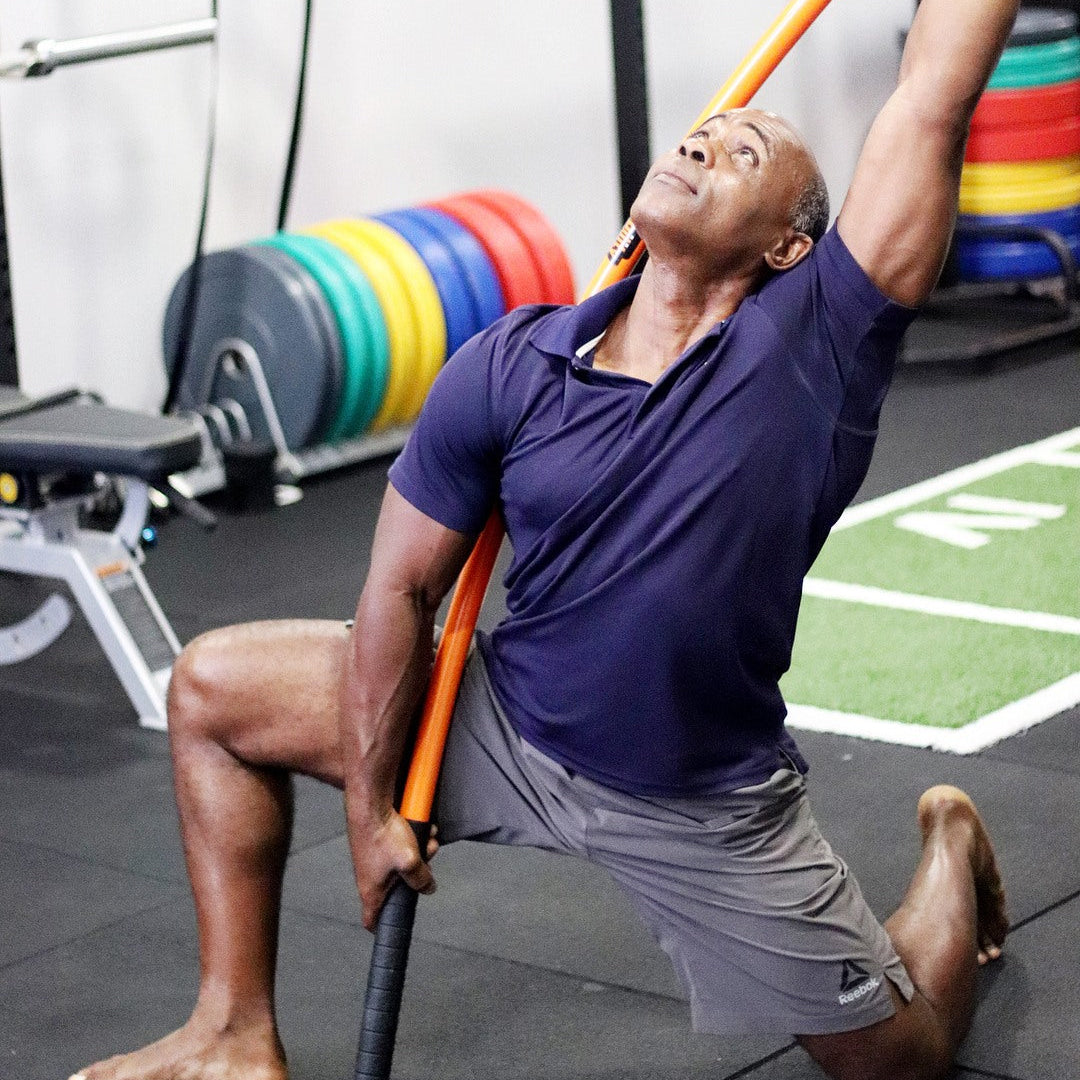 A man performing the Stick Mobility snake reach while on the floor in a forward kneeling lunge.
