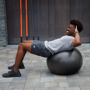 A male athlete engaging in a core workout by performing a crunch on an exercise ball, focusing on abdominal strength, stability, and control.