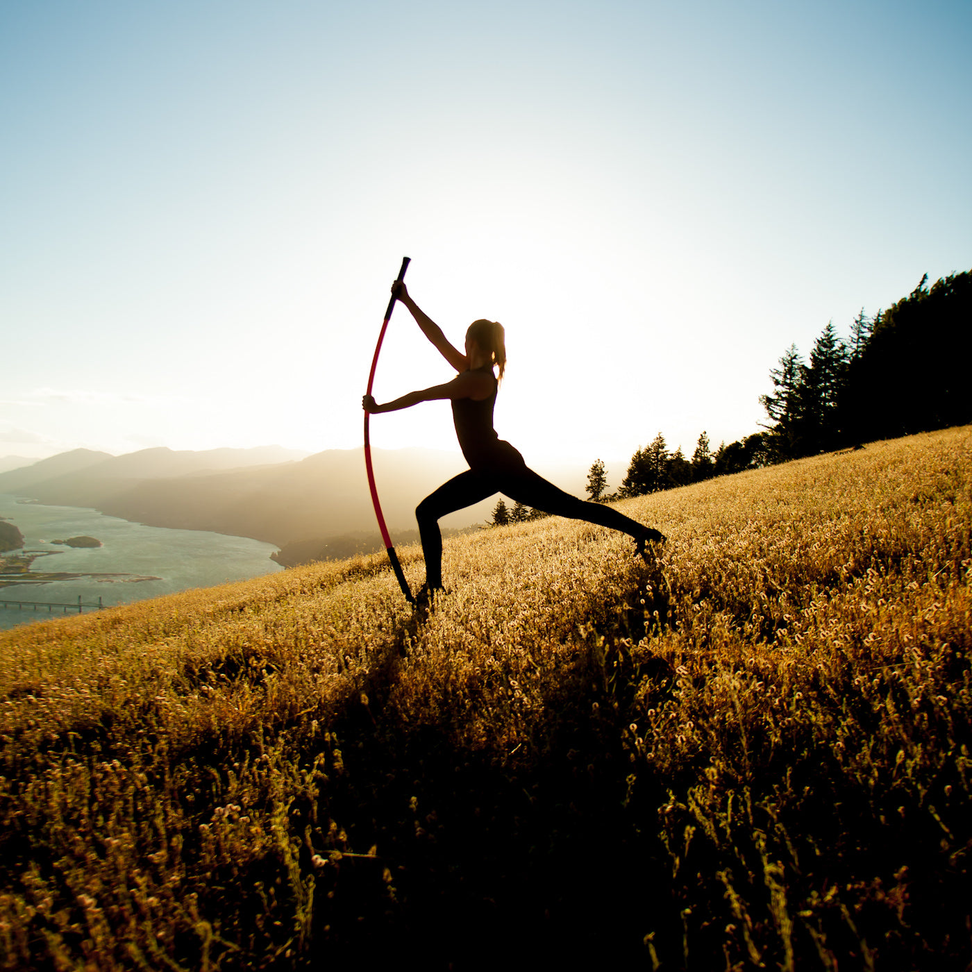 Woman on top if a mountain performing the Stick Mobility forward lunge Bow and Arrow.