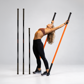 A woman in a brown sports bra and black leggings performs a movement using Stick Mobility Training Sticks. The black Training Sticks stand next to the model performing the movement.